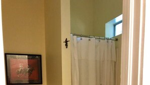 A bathroom with a toilet, a shower curtain, a framed picture on the wall, and a roll of toilet paper. - Little Lob Lolly of Point Clear located in our barn across from our stalls  (Fairhope)