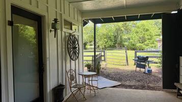 A covered porch with a table and chairs, a decorative wheel, and a view of a fenced yard with trees.