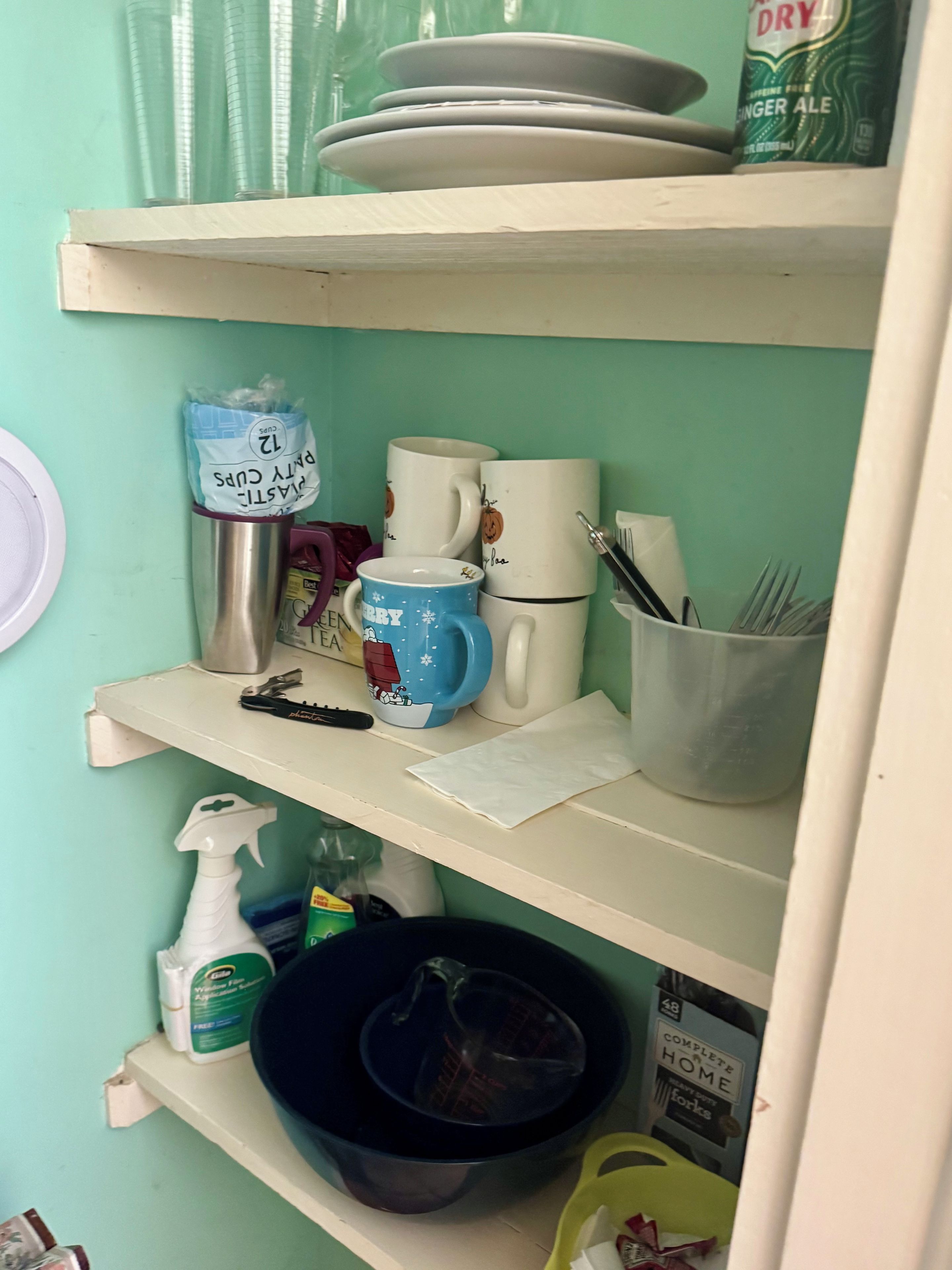 A kitchen shelf with various items including a blue mug, a white mug, a stainless steel container, and a spray bottle.