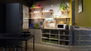 Una cocina con salpicadero de azulejos blancos, estantes de madera con utensilios de cocina, un microondas y una planta.