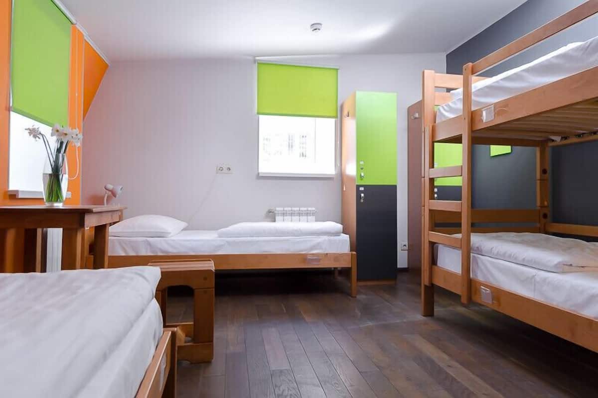 A dormitory room with bunk beds, a desk, and a window with blinds.