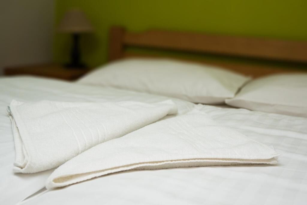 A bed with white linens and pillows, a wooden headboard, and a nightstand with a lamp.