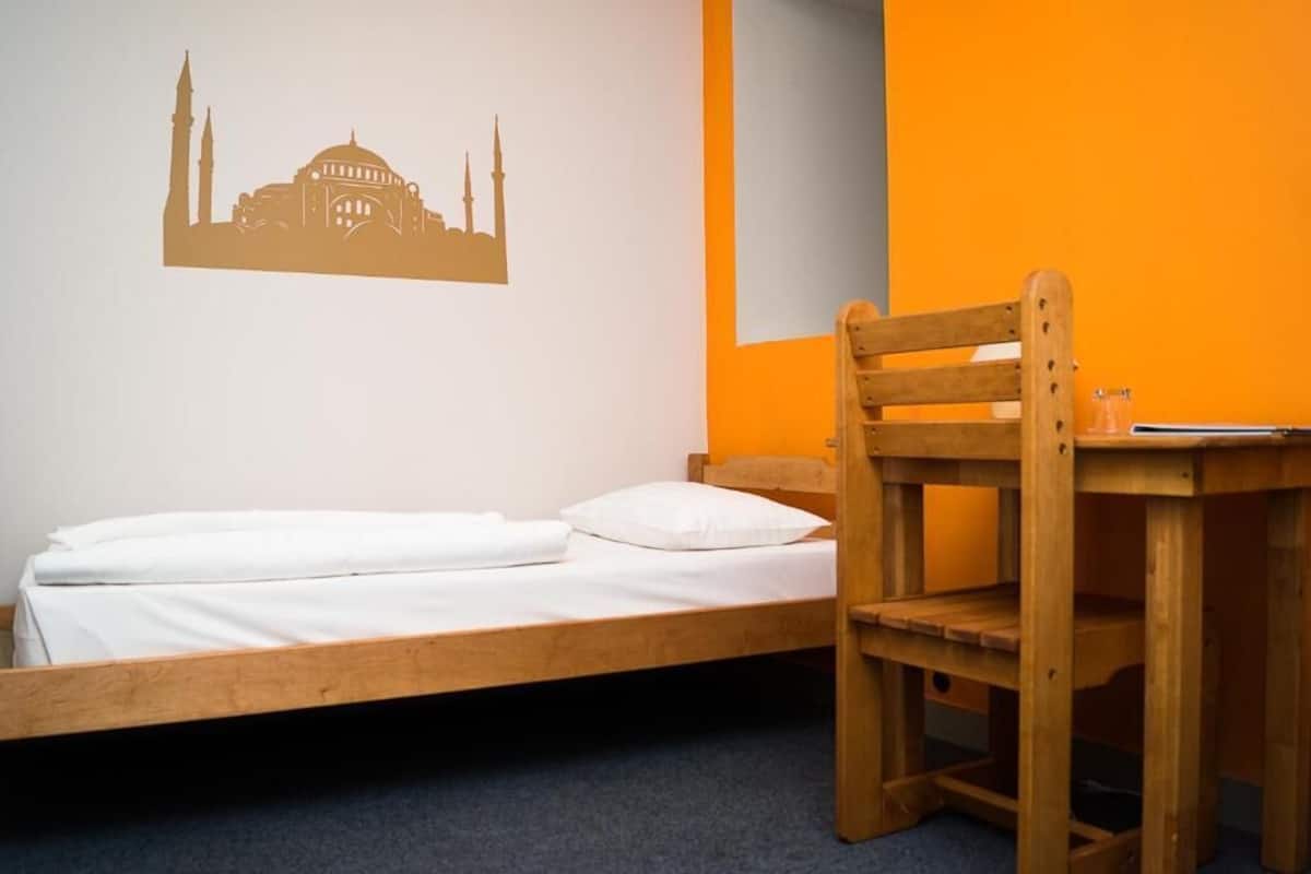 A single bed with white bedding, a wooden chair, and a small table.
