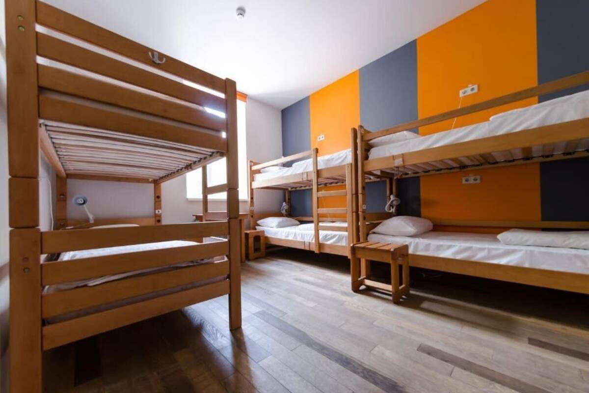 A dormitory room with bunk beds, wooden flooring, and orange and blue walls.