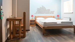 Un dormitorio con una cama, un escritorio de madera, una silla, una mesita de noche y un panel con la silueta del Teatro de Ópera de Sydney.