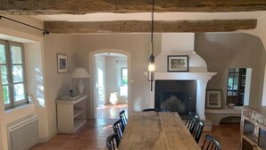 Una sala da pranzo rustica con un grande tavolo di legno, sedie, un camino e vista all'esterno attraverso una finestra.