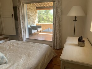 Une chambre à coucher comprenant un lit, une table de chevet, une lampe et donnant sur une terrasse extérieure avec un mur en pierre et une table.