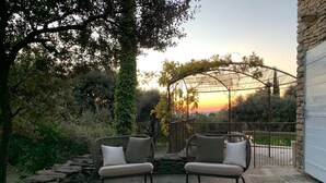 Patio esterno con mobili in vimini e tavolo, circondato da muri in pietra e vegetazione.
