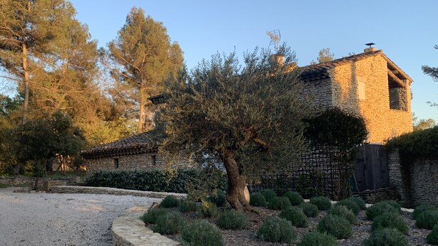 Un edificio in pietra con tetto in tegole, circondato da un vialetto sterrato e siepi curate.