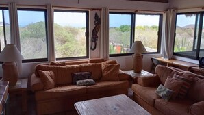 Una sala de estar acogedora con un juego de sofá, una mesa de centro de madera y dos lámparas. Amplios ventanales ofrecen vistas al exterior.