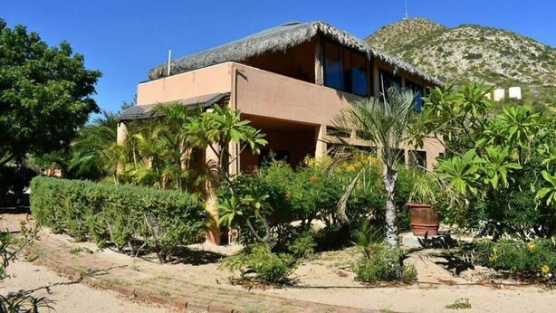 Un edificio de dos pisos con techo de paja, rodeado de abundante vegetación y un paisaje montañoso.
