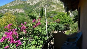 Un balcón con vistas a una montaña, rodeado de exuberante follaje y flores rosadas.