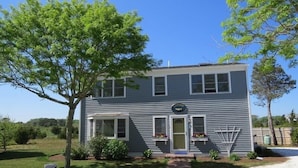 A two-story house with a front porch, a small garden, and a sign indicating a sale.