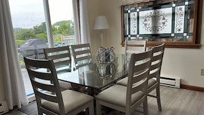 A dining area with a glass table, four chairs, a vase, and a window with decorative glass panels.
