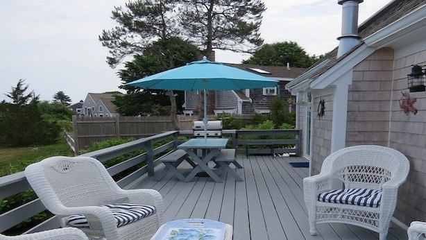 A deck with white wicker furniture, a table, and a blue umbrella.