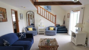 A living room with a blue sofa, two armchairs, a wooden coffee table, a staircase, and a white cabinet.