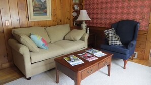 Una sala de estar con un sofá color crema, un sillón azul y una mesa de centro de madera con revistas.