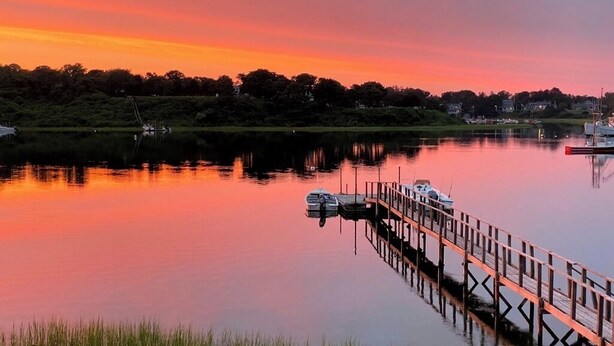 Un lac paisible au coucher du soleil, avec une jetée en bois qui s’avance sur l’eau.