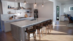 A modern kitchen with a large island, bar stools, and pendant lighting.