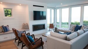 A modern living room with a fireplace, a television, and a large window offering a view of the outdoors.