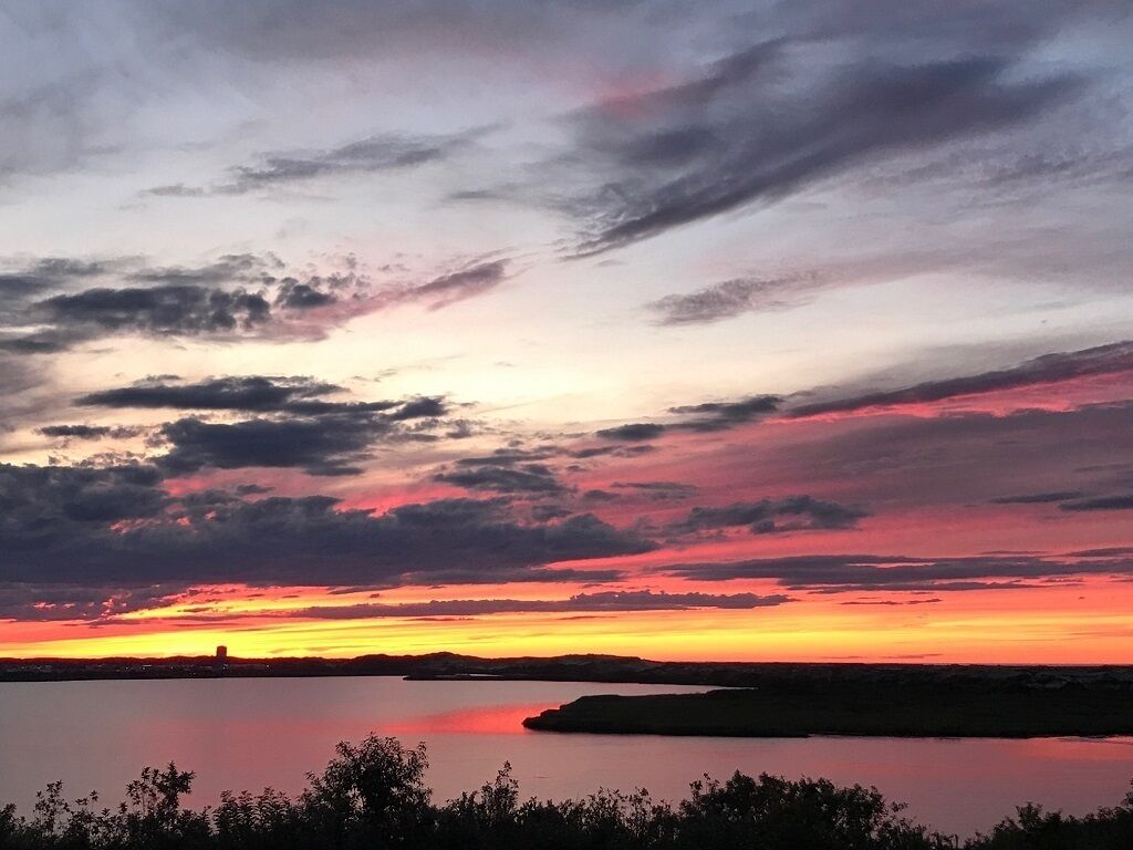 A sunset over a calm body of water with a distant shoreline.
