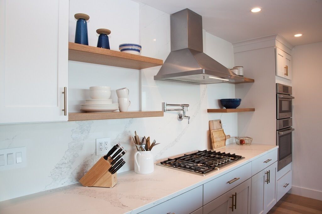 A modern kitchen with white cabinets, a stainless steel range hood, and built-in appliances.
