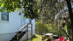 A white house with a wooden staircase leading to a deck, a picnic table, and two red Adirondack chairs. - Sweet clapboard cottage that is walk to the beach and downtown! (Chatham)