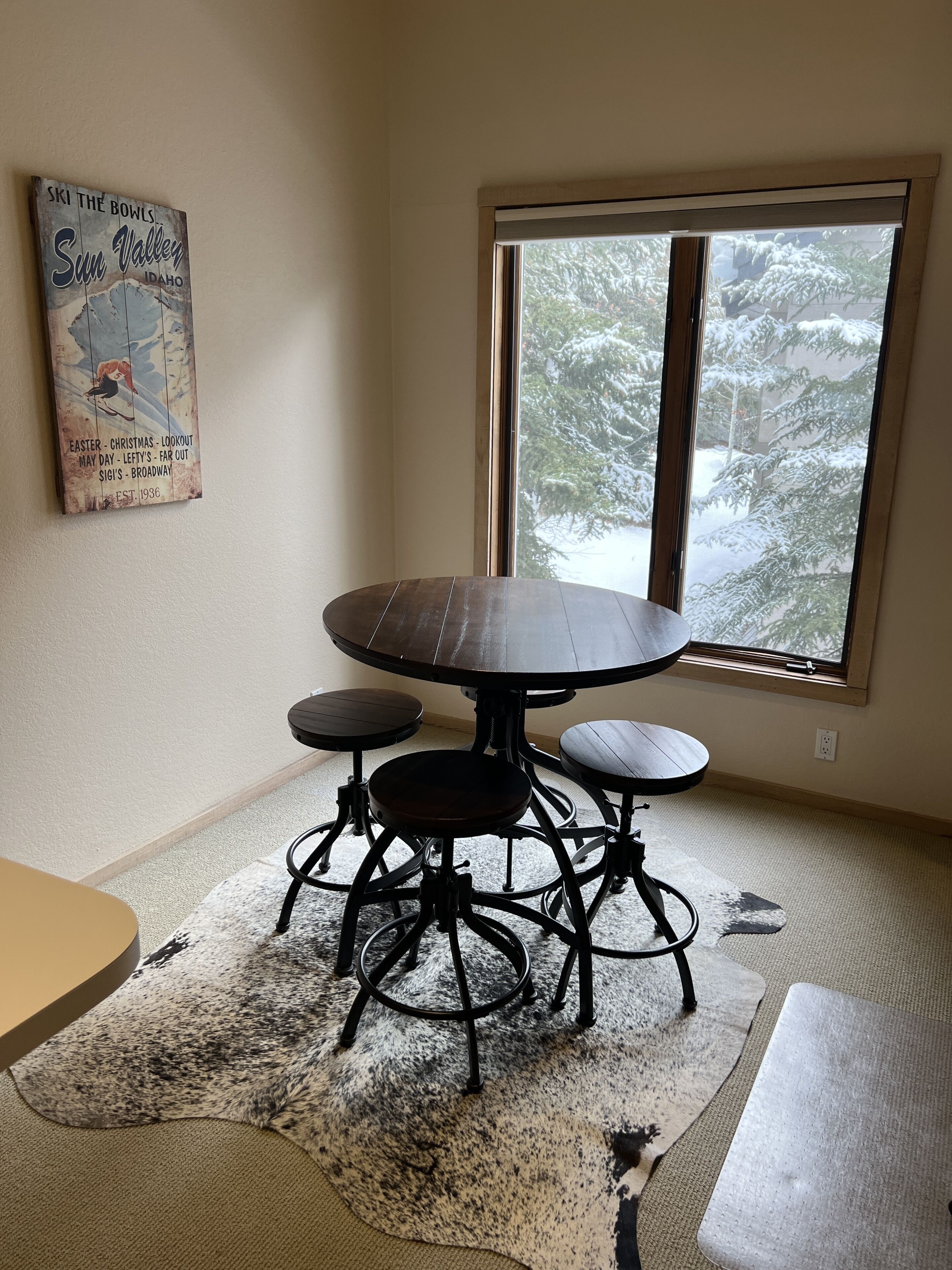A dining area with a round table and four chairs, a rug, and a poster on the wall.