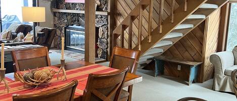 Uma sala de jantar com uma mesa e cadeiras de madeira, uma parede de pedra e uma escada de madeira.