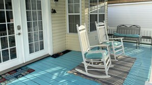 Eine überdachte Veranda mit zwei Schaukelstühlen, einem Deckenventilator und einer Fußmatte.