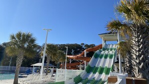 Ein Wasserpark mit einer grün-weißen Wasserrutsche, Palmen und einem Poolbereich mit Liegestühlen.
