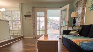 Ein geräumiges Wohnzimmer mit Holzboden, einer Couch, einem Couchtisch und einer Schiebetür zum Garten.