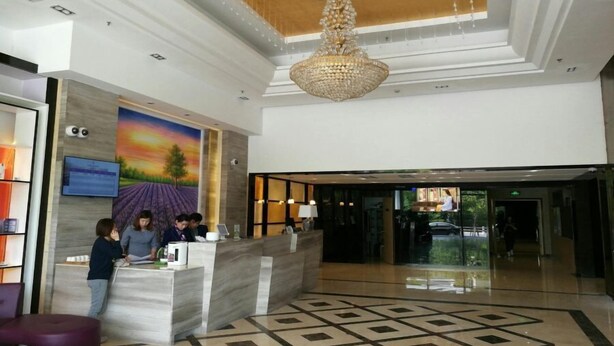 A hotel lobby with a reception desk, a chandelier, a painting of a sunset, and a patterned floor. - Lavande Hotel Shanghai Zhangjiang Guanglan Road Me (Shanghai)