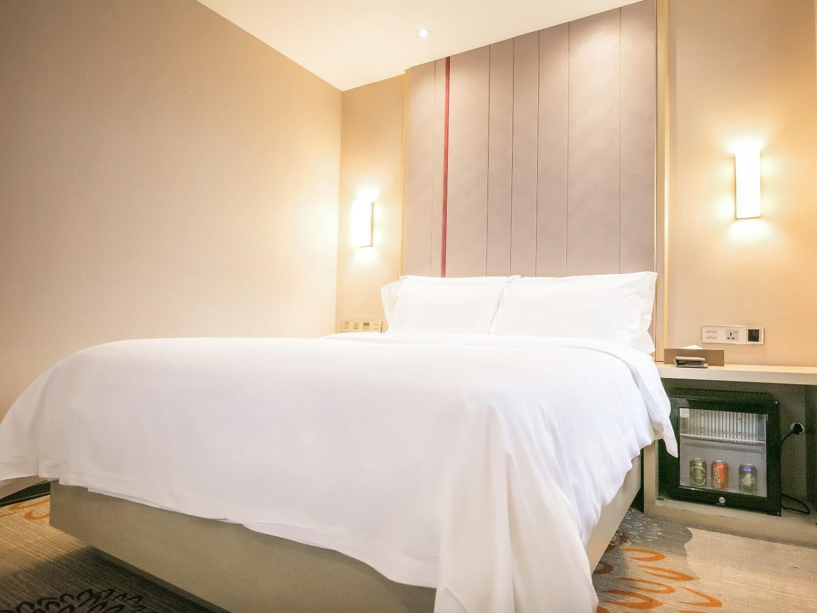 Une chambre d’hôtel comprenant un lit, des tables de chevet, une lampe fixée au mur et un mini-bar.