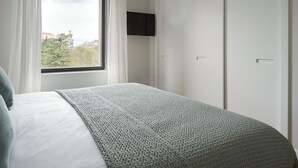 Quarto com cama, janela com cortinas, televisão de tela plana na parede e armário.