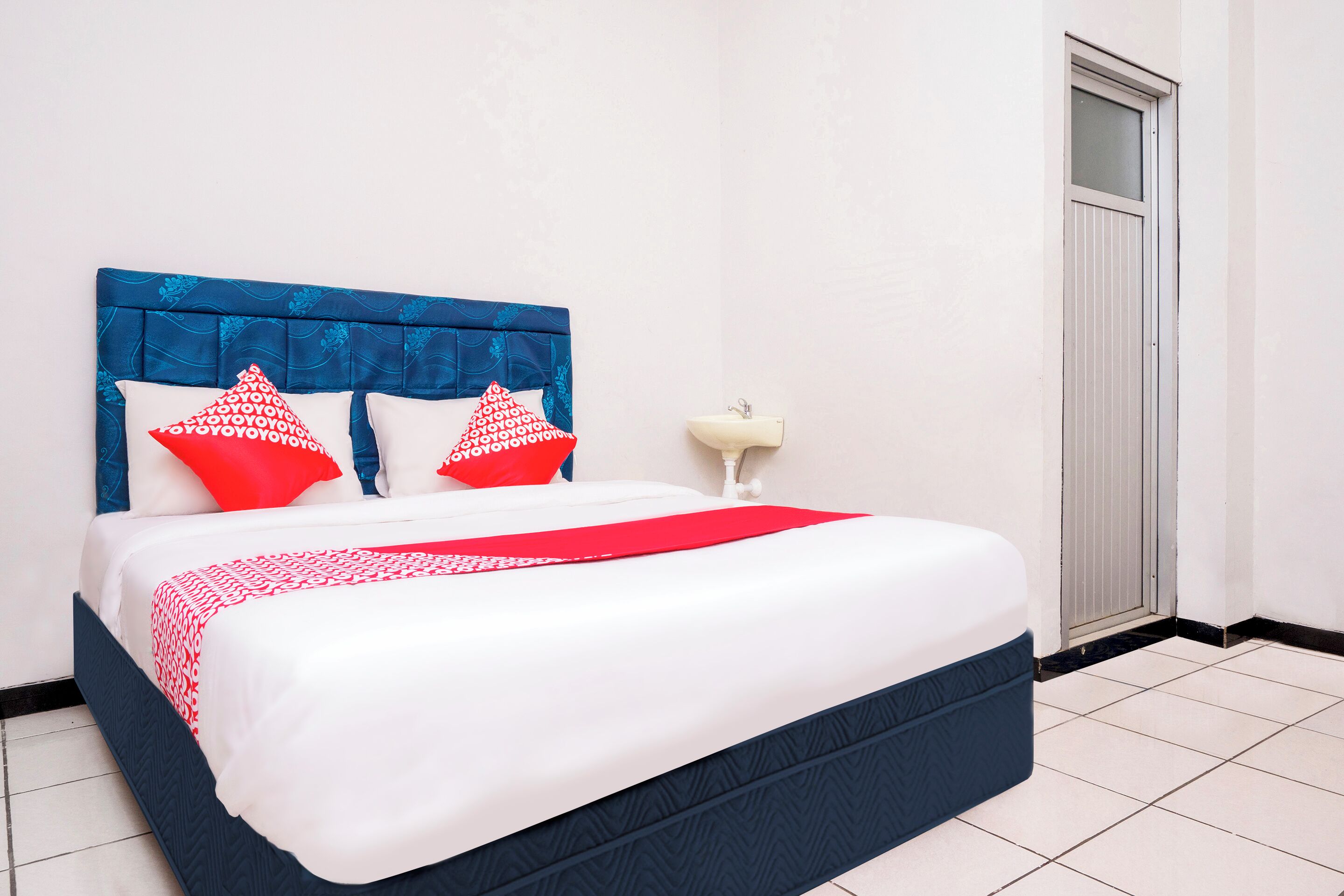 A neatly made bed with a blue headboard, white bedding, and red and white pillows.