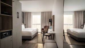 A hotel room with two beds, a desk, a chair, a mirror, and a wardrobe. - Arthotel ANA Amber (Rostock)