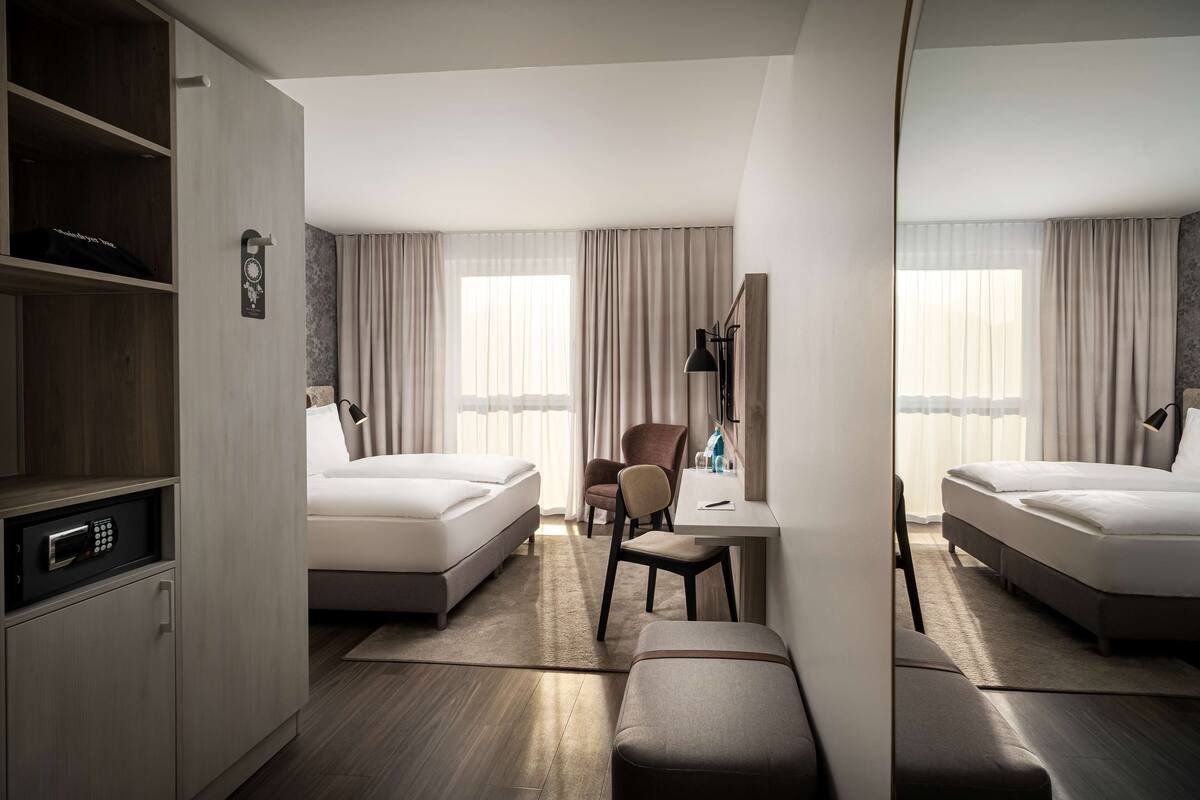 A hotel room with two beds, a desk, a chair, a mirror, and a wardrobe.