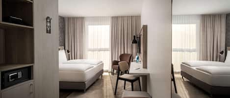 Habitación de hotel con dos camas, un escritorio, una silla, un espejo y un armario.