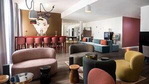 A modern living room with a large sofa, armchairs, and a dining area with red chairs. - Arthotel ANA Amber (Rostock)