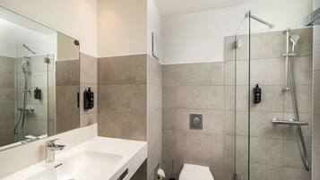 Un baño moderno con un espejo grande, un lavamanos blanco, un inodoro y una zona de ducha con paredes de vidrio.