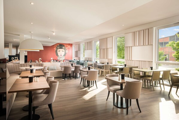 Un espace repas moderne avec des tables et des chaises en bois, de grandes fenêtres et une fresque murale.