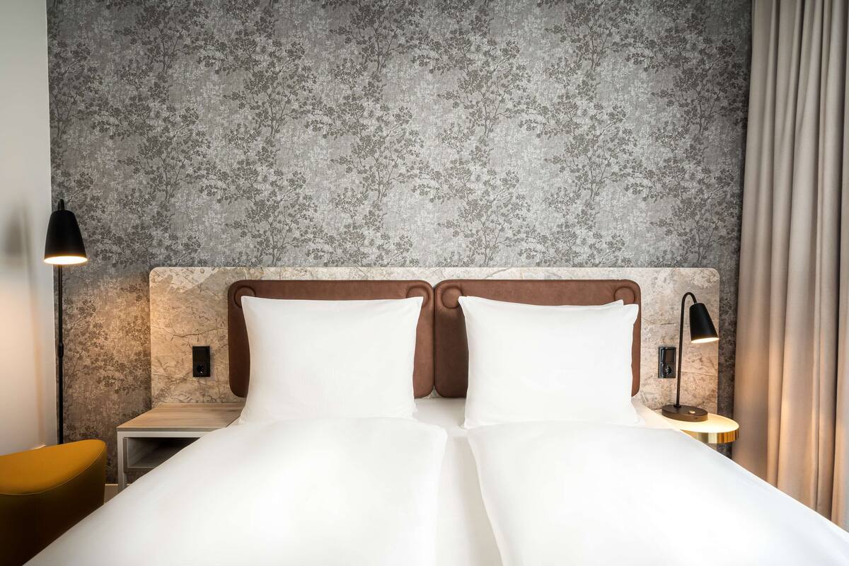 A double bed with white linens, a wooden headboard, and a nightstand with a lamp.