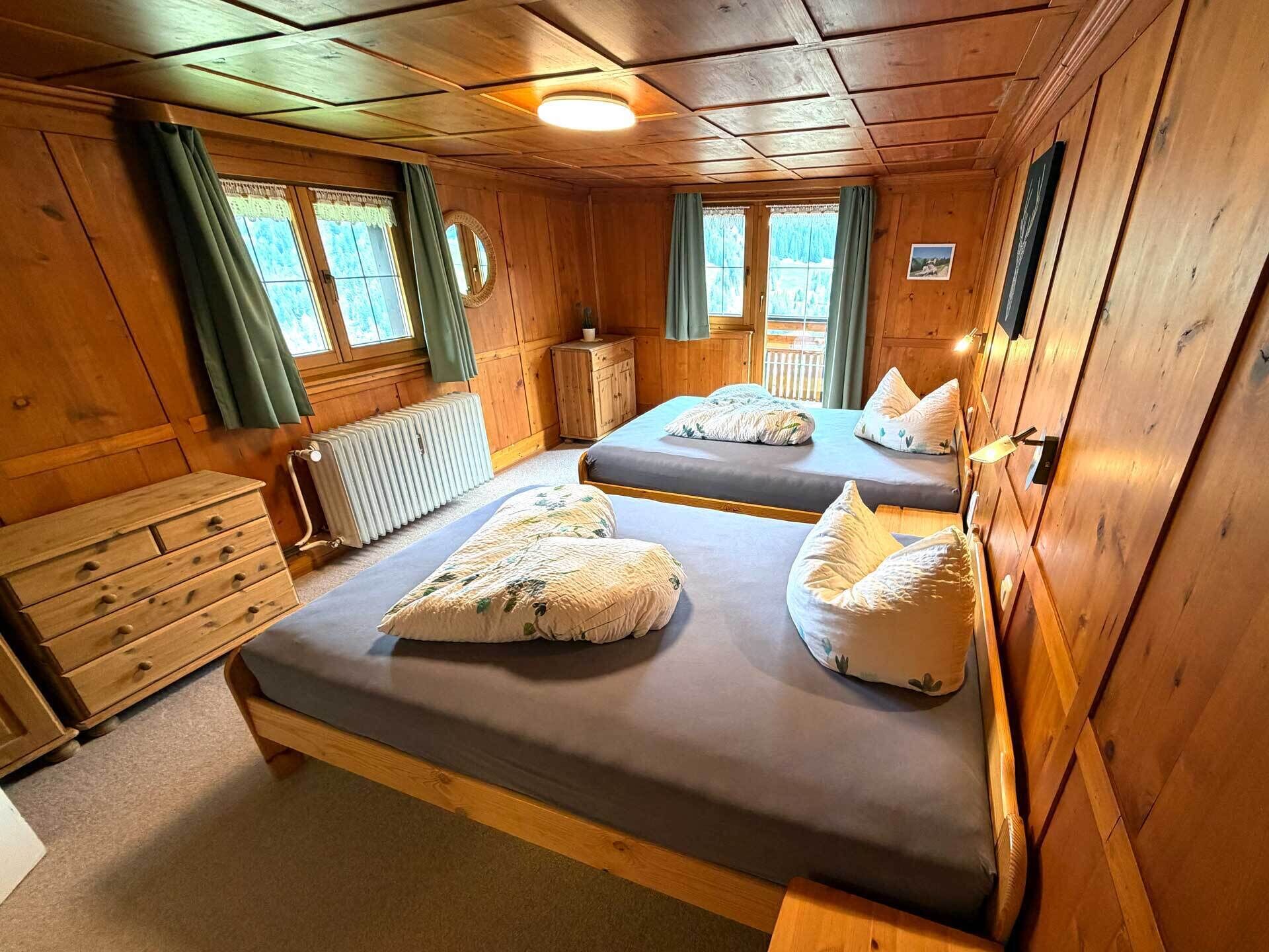 Eine Holzhütte mit zwei Betten, einem Schmuckkästchen, einem Heizkörper und einem Fenster mit Vorhängen.