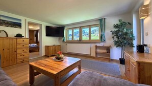 Una sala de estar acogedora con una mesa de centro de madera, un sofá, un televisor y una ventana con vista a la montaña.