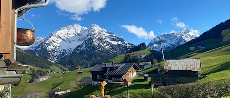 Un pueblo rural con casas tradicionales, una estructura de madera con una olla de cobre y montañas nevadas al fondo.