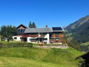 Una casa moderna de dos pisos con base de piedra, balcones de madera y un panel solar en el techo.