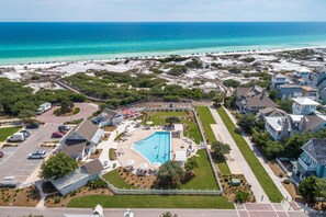 An aerial view of a coastal resort with a swimming pool, beachfront, and residential buildings.