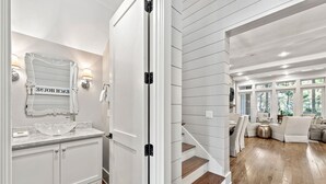 Un intérieur moderne avec un meuble-lavabo blanc dans la salle de bain, un miroir doté d’un cadre décoratif et un escalier menant à un espace de vie offrant une vue sur la verdure.