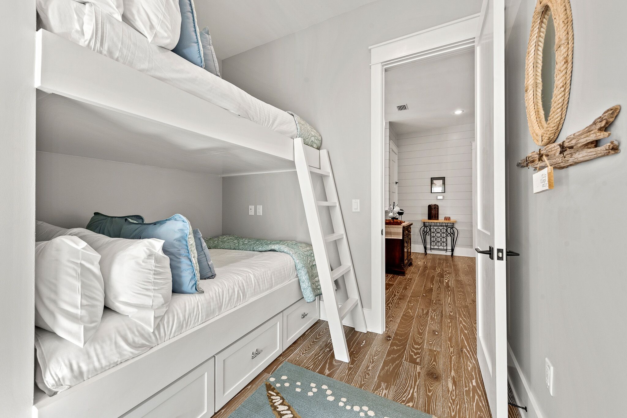 A bunk bed room with a ladder, a desk with a chair, and a decorative wall hanging.
